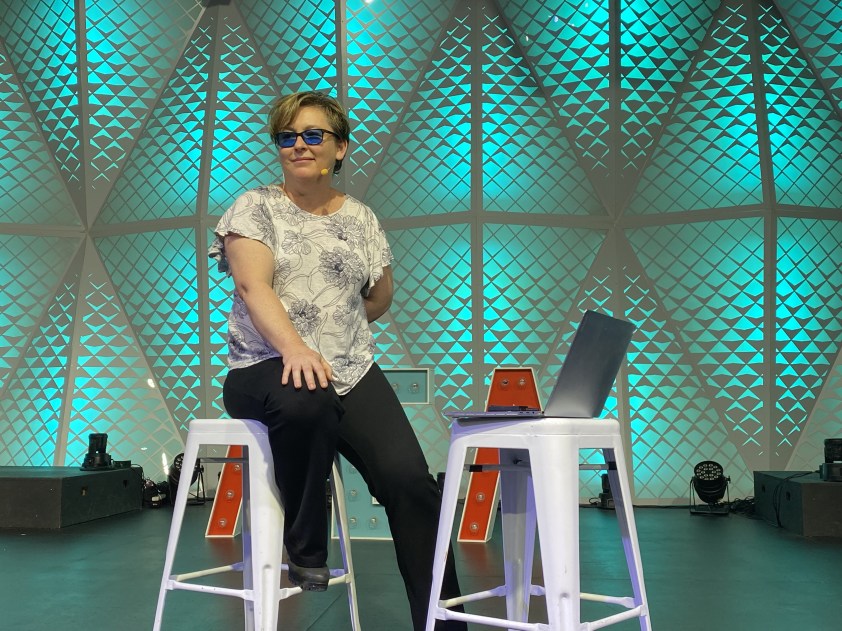 Dr Jodie sits on a stool on stage, holding a microphone 